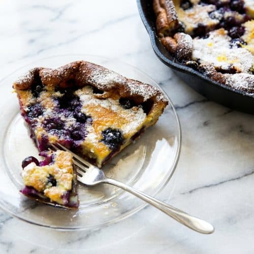 Puffed blueberry lemon dutch baby in a cast iron skillet with browned butter and lemon sugar crust.