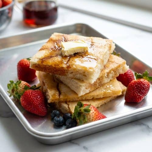 Golden brown sheet pan pancakes topped with maple syrup, showing the crispy broiled edges from the brown butter technique.