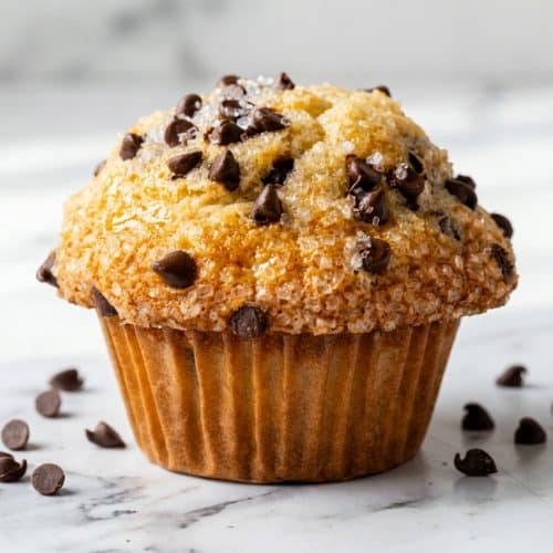 Tall bakery-style chocolate chip muffins baked with brown butter, featuring thick domed tops and melted chocolate.