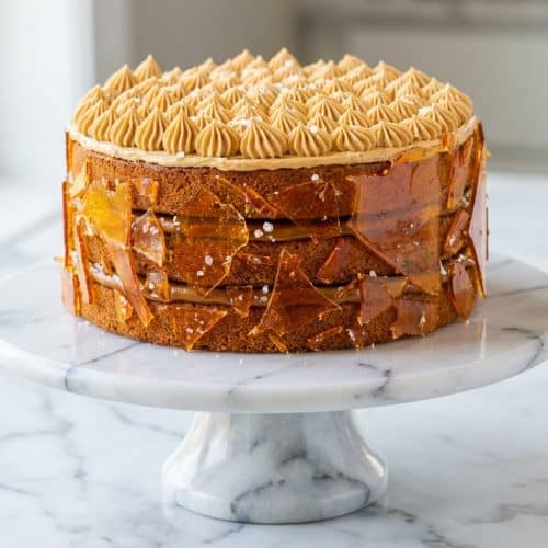 Tall layered dulce de leche cake with brown butter cake layers, frosting, and flaky sea salt sprinkled between each tier.