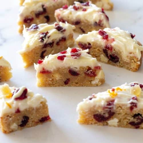 Sliced cranberry bliss bars recipe with browned butter blondie base, cream cheese frosting, and crystallized ginger pieces.