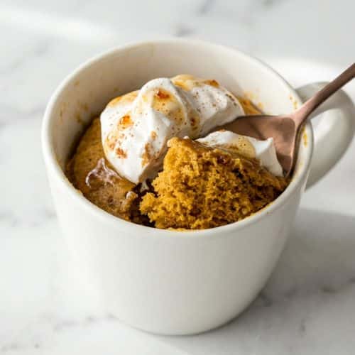 Moist pumpkin mug cake topped with whipped cream, infused with nutty browned butter in a microwave-safe mug.