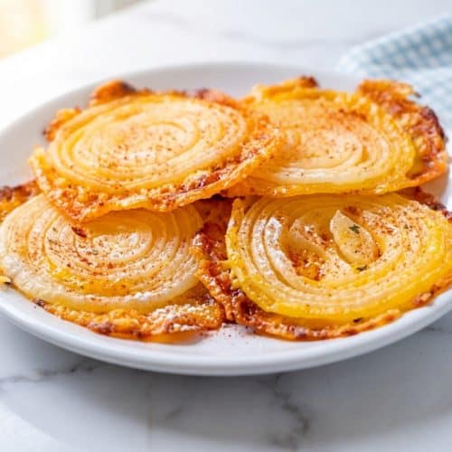 A sheet of parchment paper covered with golden-brown Cheesy Onion Crisps, showcasing the extra crispy texture from the double-crunch dusting.