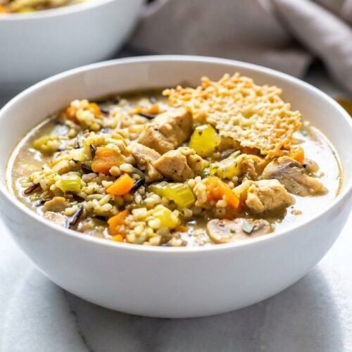 Creamy chicken and wild rice soup topped with a savory Parmesan crust umami bomb in a white ceramic bowl.