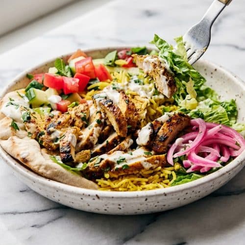 Golden chicken shawarma bowl featuring spiced chicken thighs served over yellow turmeric rice and drizzled with the street cart style white sauce twist