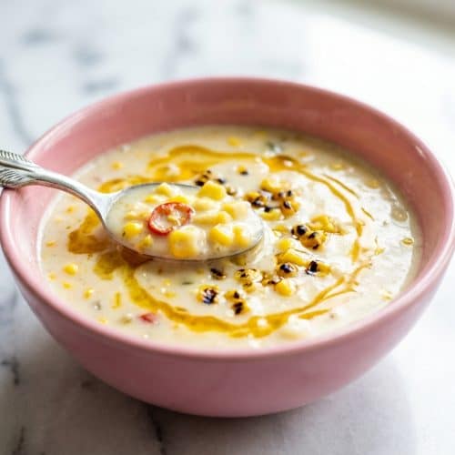 Bowl of creamy corn chowder with chilies garnished with herbs, highlighting the rich color from the corn cob broth infusion.