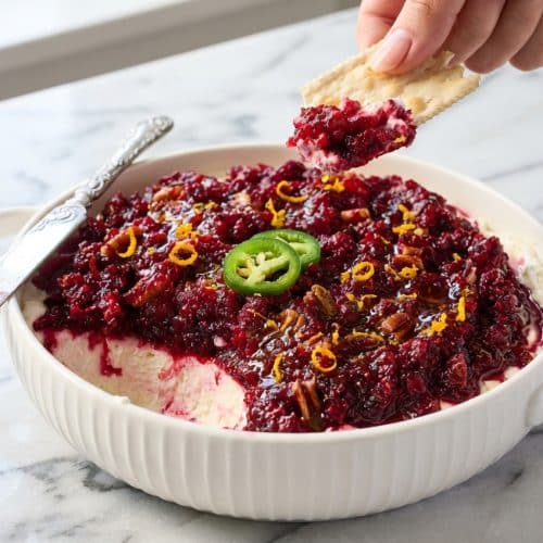 Creamy cranberry jalapeno cream cheese dip topped with hot honey and fresh orange zest in a festive holiday bowl.