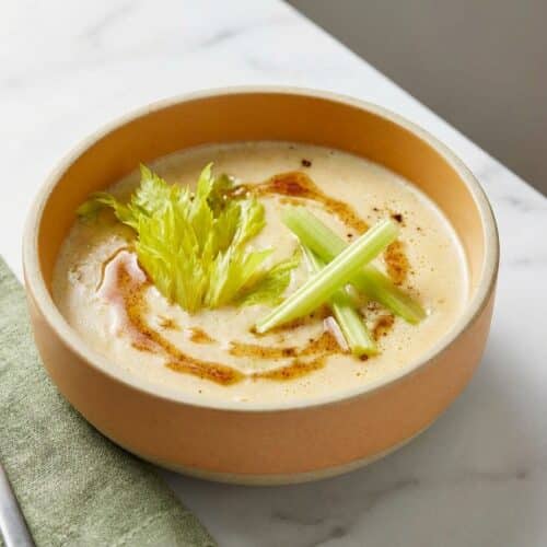 Cream of celery soup topped with brown butter nutmeg infusion and reserved celery batons in a ceramic bowl.