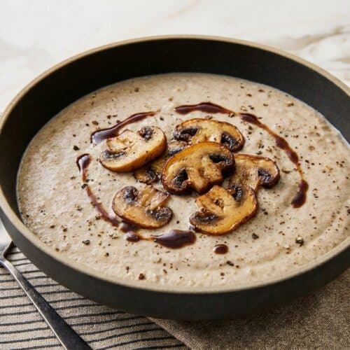 Velvety cream of mushroom soup in a bowl showing deep color from the umami-bomb browning technique.