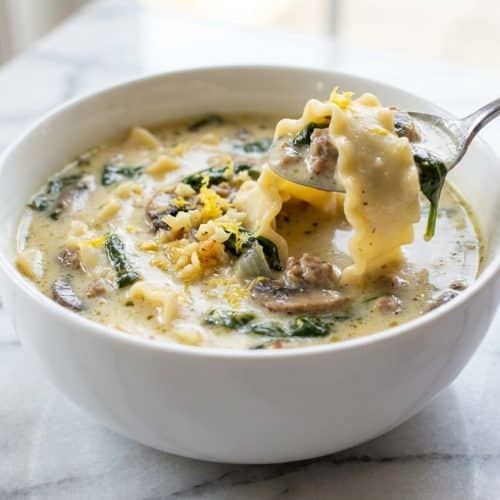 A white bowl filled with creamy alfredo lasagna soup, infused with roasted garlic and topped with fresh parsley and a twist of lemon zest.