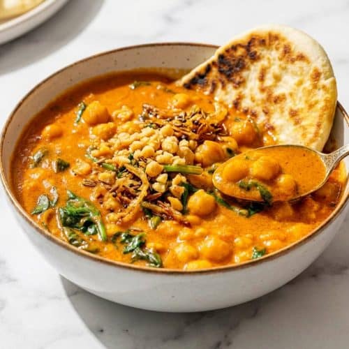 Overhead view of a rich chickpea curry in a pot featuring the smashed chickpea texture and golden fried aromatics on top