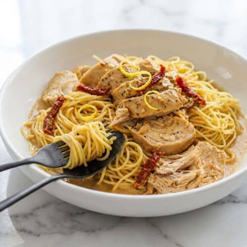 Creamy crockpot angel chicken over pasta with a sun-dried tomato and lemon brightener garnish.