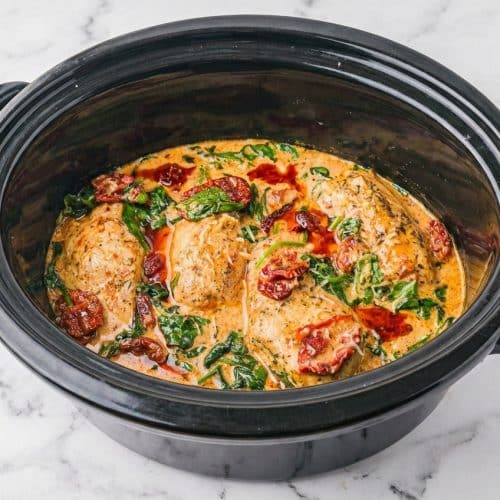 Golden crockpot tuscan chicken recipe seared in sun-dried tomato oil with baby spinach in a creamy sauce.