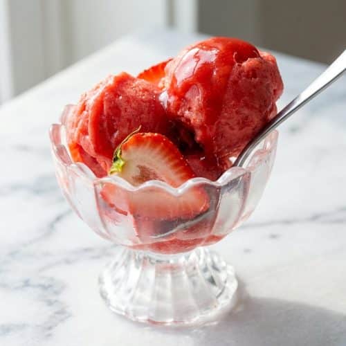 Two vibrant scoops of intensely colored strawberry sorbet in a glass bowl, showcasing a super smooth, concentrated texture.