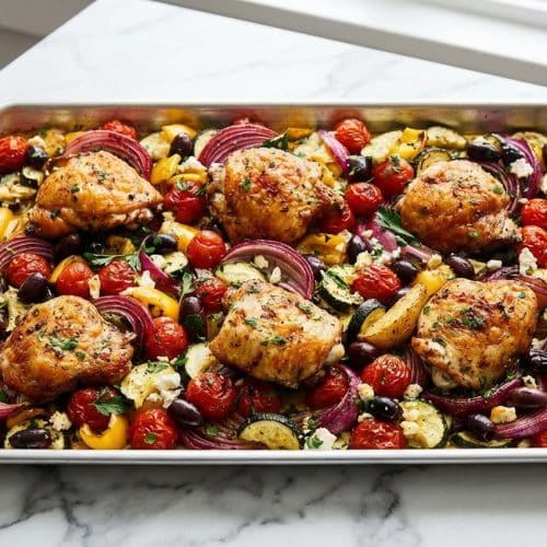 Golden roasted greek sheet pan chicken thighs served with crispy potatoes cooked using the staggered method and tender zucchini.