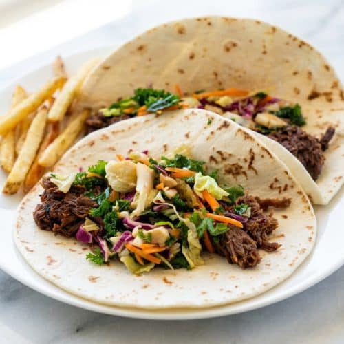 Crispy-end skillet finish korean beef tacos topped with spicy kimchi and sriracha mayo on warm tortillas.