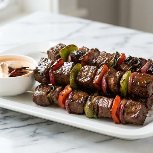 Grilled Marinated Steak Kabobs on a platter, coated in a glossy post-grill glaze with tender, velveted beef and vegetables.