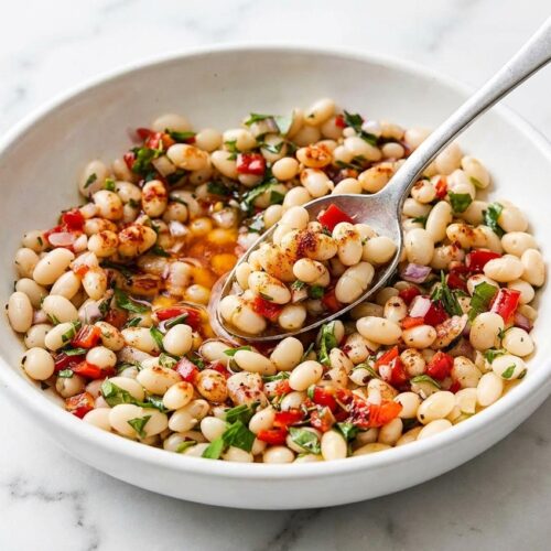 Creamy marinated white beans finished with a vibrant smoked paprika and warm oil bloom in a shallow bowl.