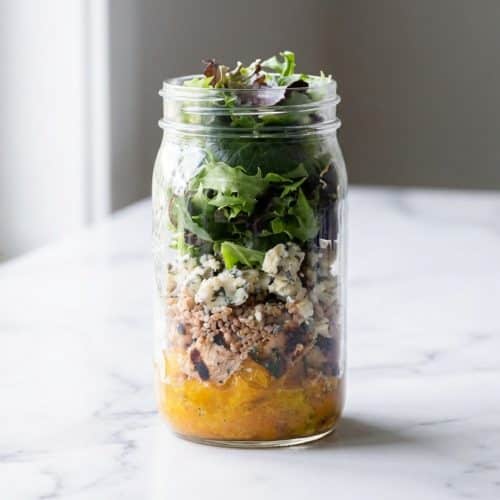 Layered mason jar salad showcasing the grain-barrier seasoning method with quinoa protecting fresh leafy greens.