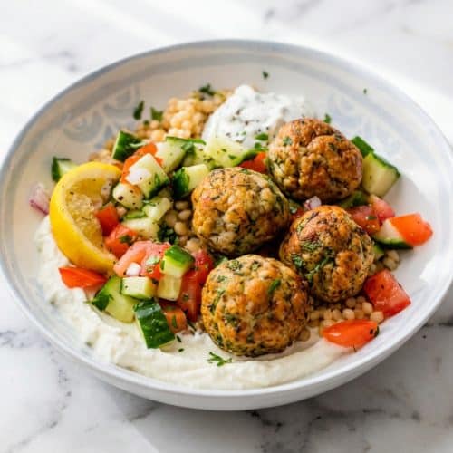 Golden brown turkey meatballs resting on a creamy whipped feta bed in a vibrant Mediterranean Meatball Bowl with cucumbers and herbs