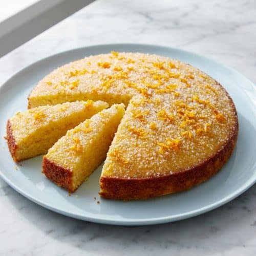 Golden orange olive oil cake on a ceramic plate, highlighting the rich color achieved by the sugar-zest massage technique.