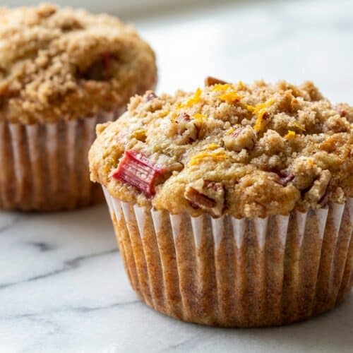 Golden rhubarb muffins topped with orange-scented streusel and toasted pecans in paper liners.