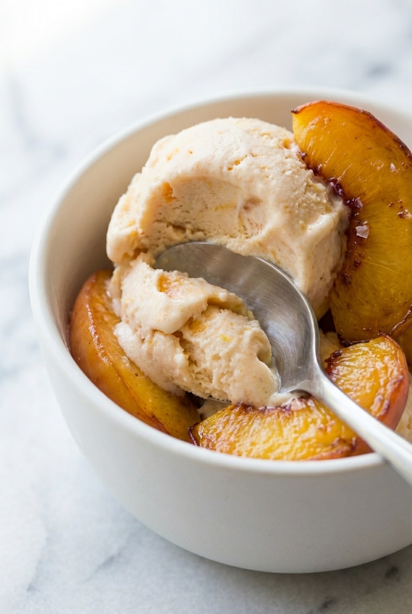 A metal scoop digging into a batch of peach frozen yogurt showing a smooth, soft-serve consistency.