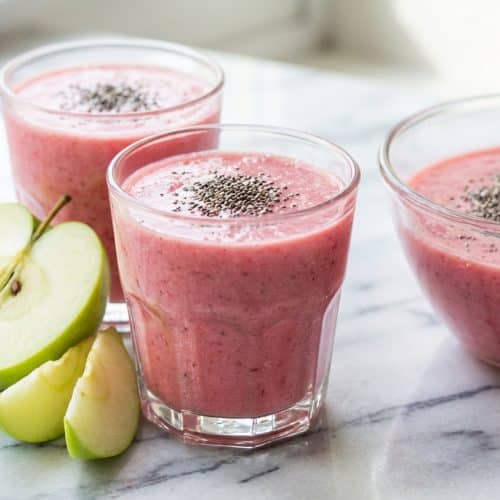 Glass of pink salt detox smoothie blended with fresh green apple and chia seeds, topped with a lemon wedge.