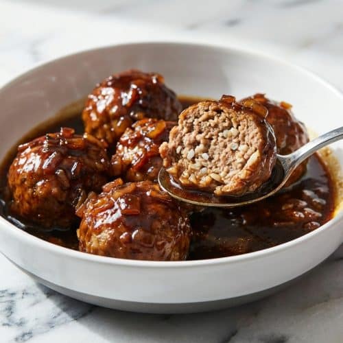 Tender porcupine meatballs simmering in a rich tomato sauce enhanced with balsamic vinegar and sautéed aromatics in a skillet