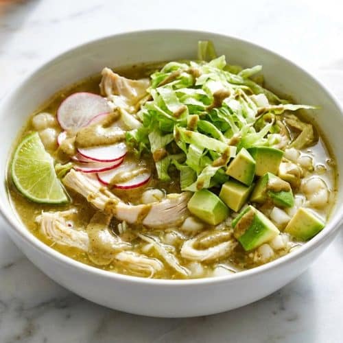 A bowl of vibrant pozole verde topped with a creamy toasted pepita emulsion and fresh radish slices.