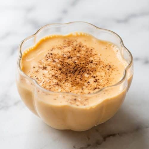 Glass of creamy Pumpkin Eggnog garnished with fresh nutmeg, highlighting the rich color achieved by the bloomed pumpkin technique