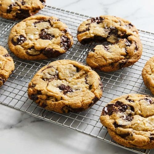 Golden brown sea salt chocolate chip cookies stacked on a plate showing the thick texture achieved by the pre-scoop aging technique.