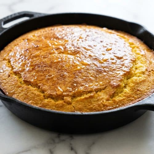 Golden skillet cornbread with a crispy browned honey butter crust in a seasoned cast iron skillet.