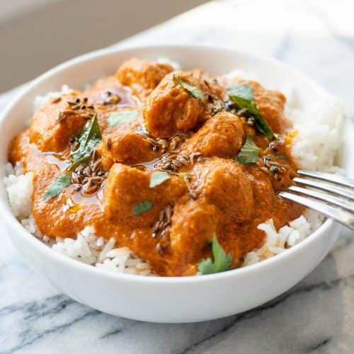 Slow cooker chicken tikka masala in a bowl featuring a vibrant spiced-oil tadka bloom and fresh cilantro.