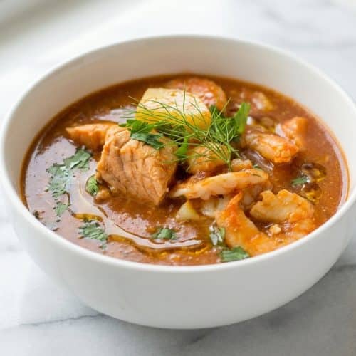 Slow cooker seafood stew in a bowl topped with aromatic fennel and a rich brown butter drizzle.