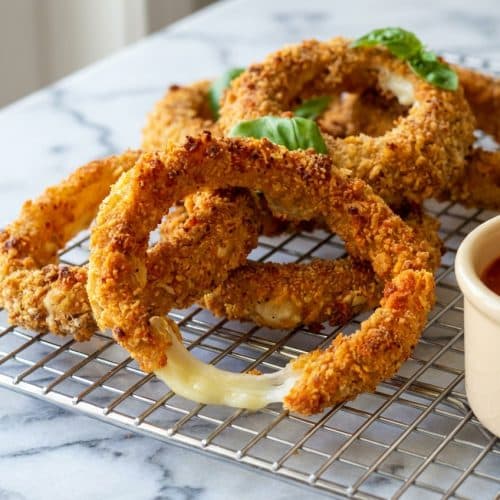 Golden brown mozzarella stick onion rings piled high featuring a spicy chip crust and melted cheese center.
