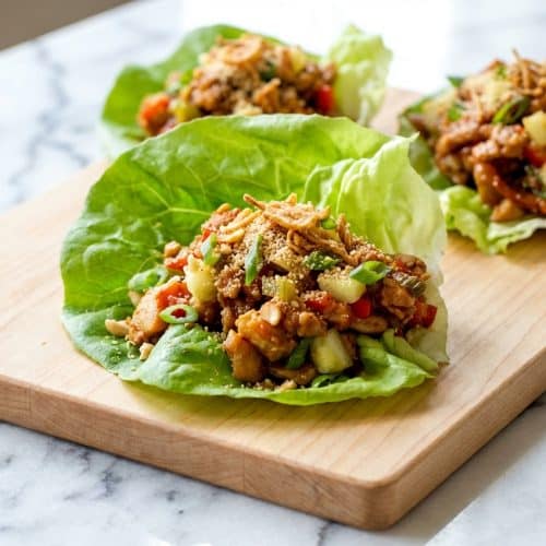 Platter of Thai Chicken Lettuce Wraps topped with crispy fried shallots and toasted rice powder on fresh butter lettuce leaves