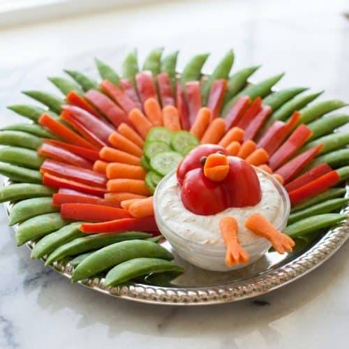 A festive turkey veggie tray with colorful vegetable 'feathers' and a clever 3D bell pepper head centerpiece.