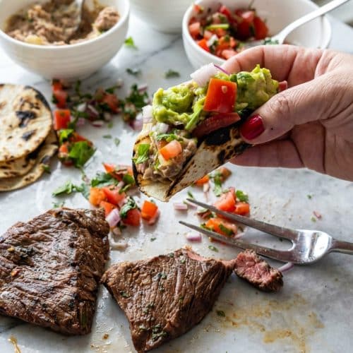 Platter of Carne Asada Tacos filled with juicy grilled steak marinated with soy sauce and bloomed spices topped with onions and cilantro