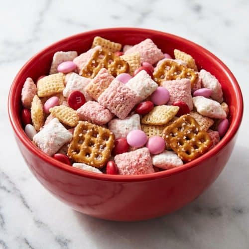 Bowl filled with pink and white valentine chex mix coated in strawberry shortcake dusting and mixed with salty pretzels