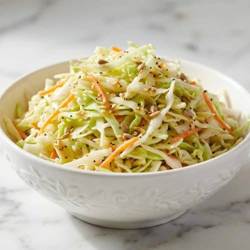 Crisp vinegar coleslaw recipe featuring shredded cabbage and carrots tossed in a toasted seed warm emulsion.