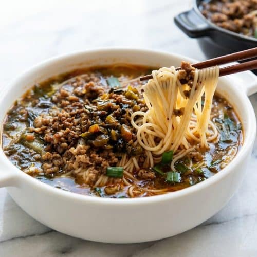 Yunnan rice noodle soup featuring an umami-seared pickle base and vibrant garlic chives in a savory broth.