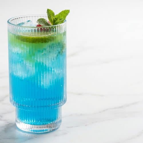Vibrant blue raspberry energy drink featuring a zesty lime juice twist over crushed ice.