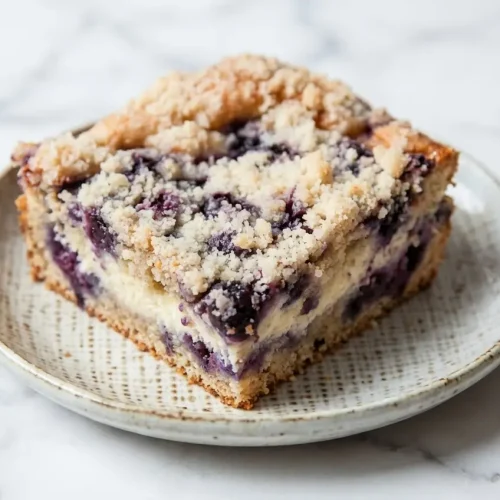 A slice of Blueberry Cream Cheese Coffee Cake with lemon-rubbed sugar, topped with toasted almond streusel and flaky sea salt.