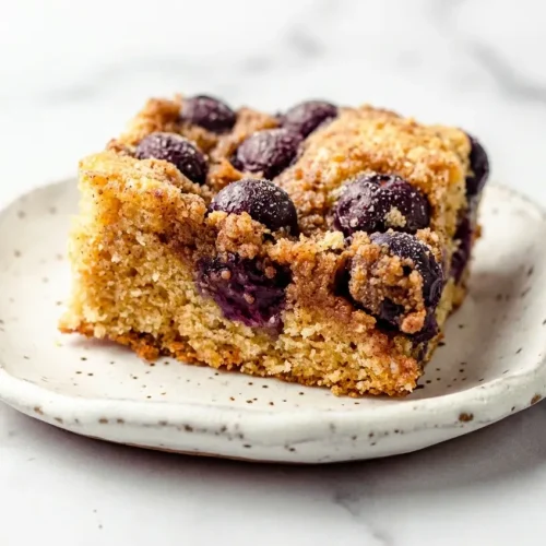 A slice of blueberry sour cream coffee cake topped with brown butter cardamom streusel next to fresh blueberries.