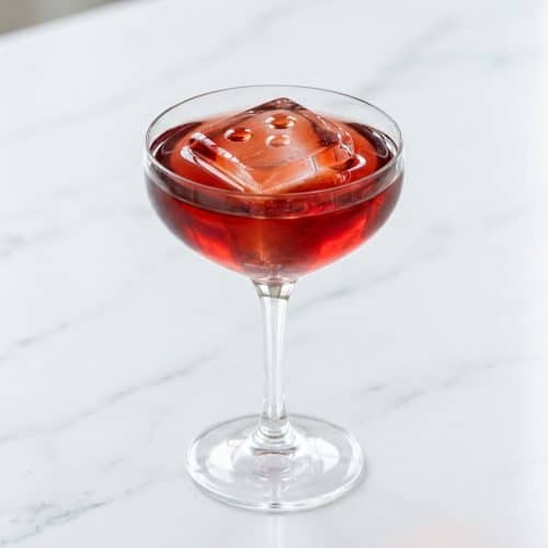 Broken Plane Cocktail served in a coupe glass over a slanted clear ice cube, finished with saline drops.