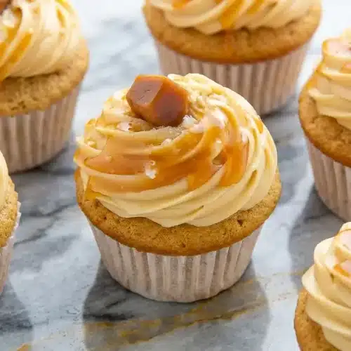 Salted caramel cupcakes with nutty brown butter frosting and a glossy caramel drizzle on a white ceramic plate.