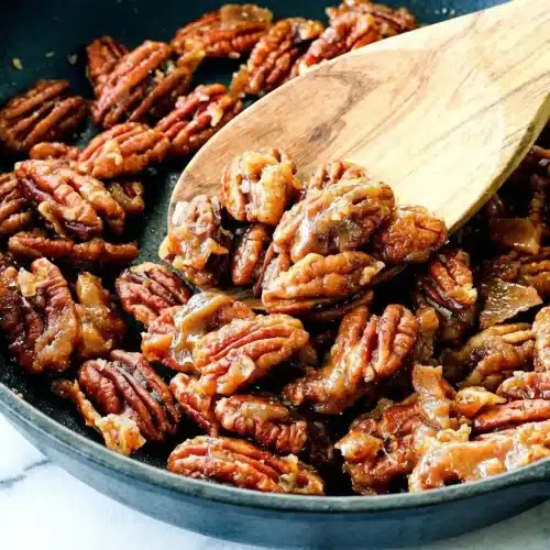 Golden brown Candied Nuts resting on parchment paper, coated in a glossy caramelization from a water and vanilla sugar glaze.