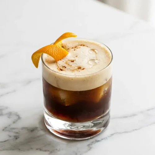 Frothy carajillo with tequila in a rocks glass, garnished with an expressed orange peel and a hint of molé bitters.