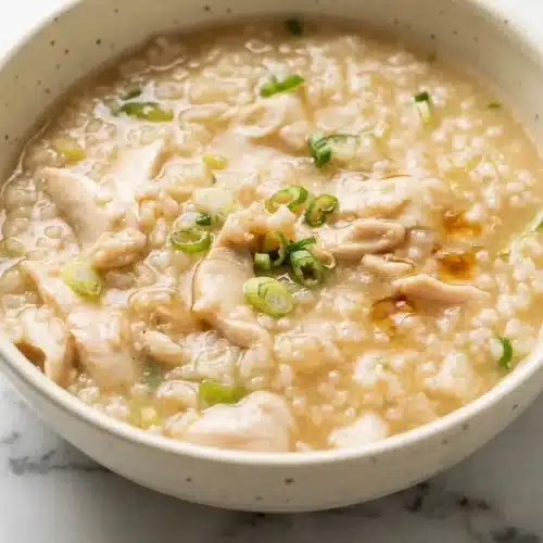 Creamy bowl of our chicken congee recipe made with collagen-rich bone broth and frozen rice, garnished with fresh scallions.